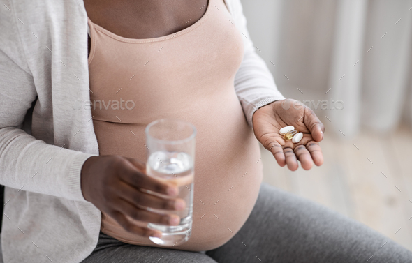 Prenatal Vitamins And Supplements. Unrecognizable black pregnant woman taking pills and water