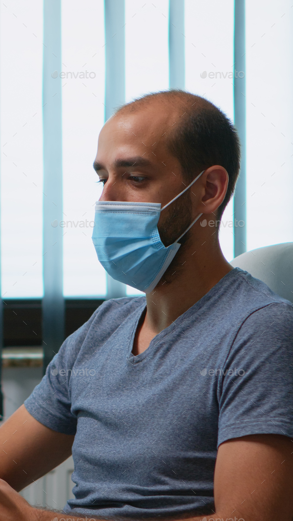 Man with protective mask during video meeting sitting alone in office. Freelancer working in new normal workplace chatting talking having virtual conference, webinar, using internet technology