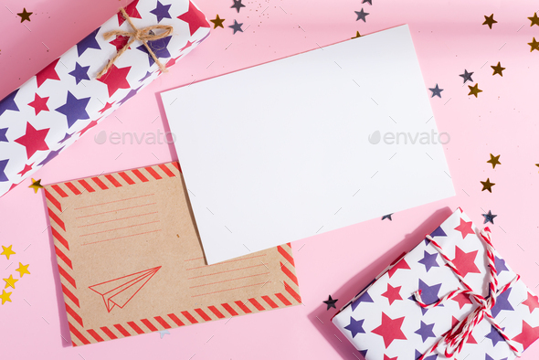 Congratulation Christmas card with colorful different gift boxes, mock-up blank letter to Santa and envelope on a light pink background with shadows, copy space . Top view.