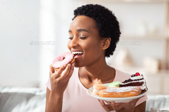 Diet breakdown, cheat meal and imbalanced nutrition. Young black woman with plate of sweets eating