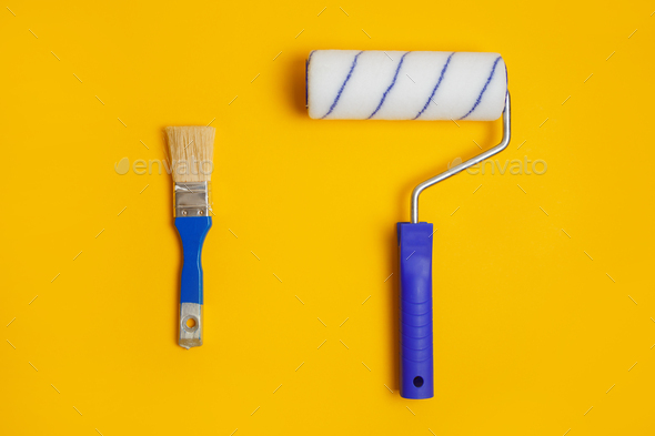 Paint roller and brush isolated on yellow. Painter tools for working with paint.