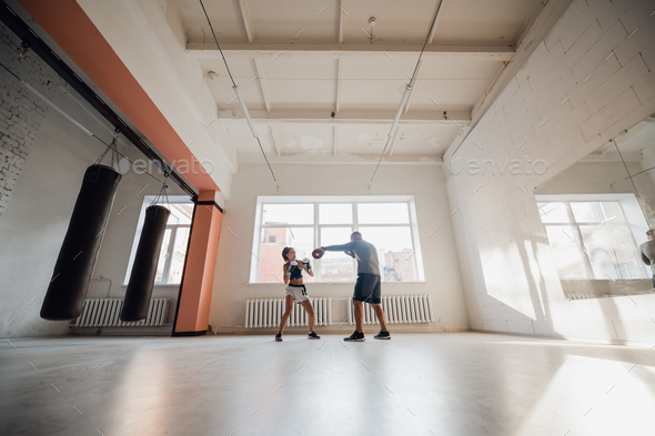 A man and a woman sparring partners train in the fighters training hall in boxing gloves with paws