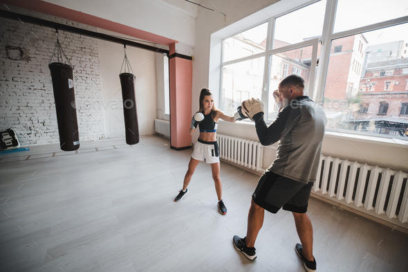 A man and a woman sparring partners train in the fighters training hall in boxing gloves with paws.