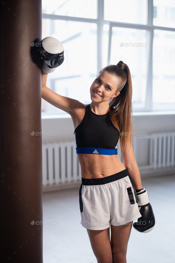 Cute girl posing for a photo in boxing gloves on the background of punching bags - Stock Photo - Images