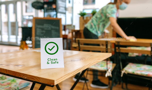 Clean and Safe sign placed on a table with waitress cleaning in the background