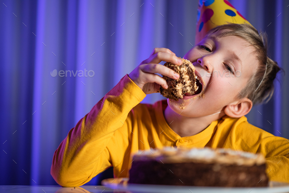 Happy child takes a piece of celebration cake and then bite it. - Stock Photo - Images