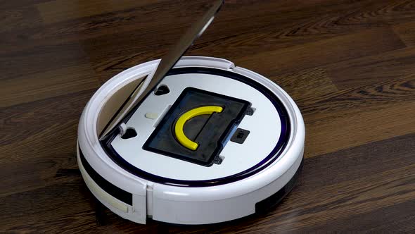 A Dirty Filter Is Pulled Out of a Vacuum Cleaner Robot. Automatic White Round Vacuum Cleaner alt
