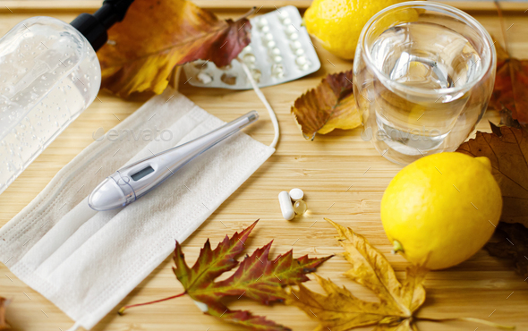Vitamin D, vitamin C and zinc pills with face mask, disinfection gel, lemons and fall leaves