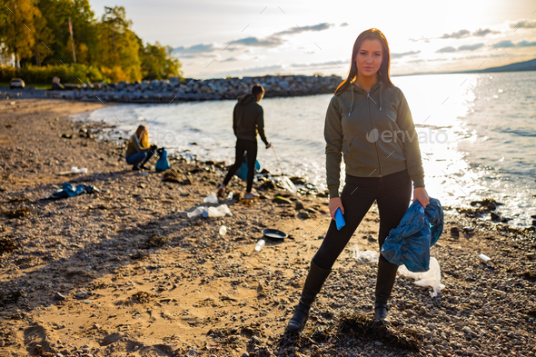 Serious young woman cleaning beach for plastic with volunteers during sunset - Stock Photo - Images