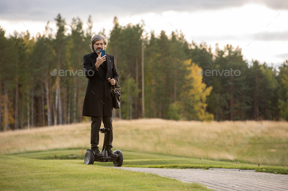 Contemporary grey-haired businessman in black coat using smartphone - Stock Photo - Images