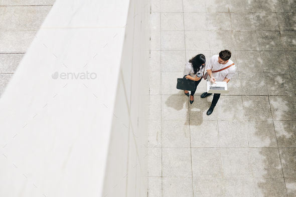 Young coworkers standing outdoors and discussing information on laptop screen, view from above