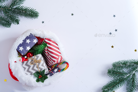 Christmas background with red Santa’s hat filled colorful different gift boxes and candies on a light grey background decorated green fir twigs, copy space. Top view. Greeting card.