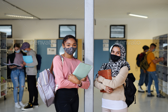 Young students friends with face masks back at college or university, coronavirus concept.