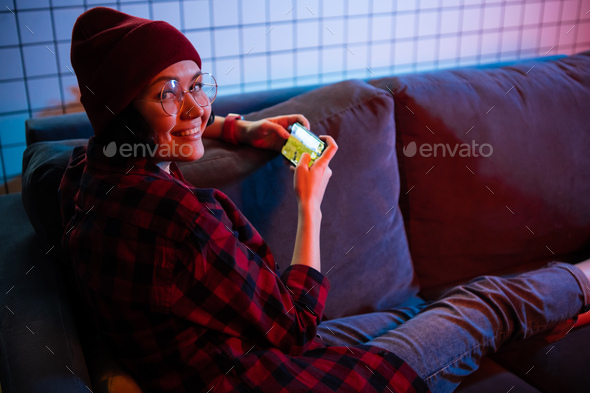 Teenager girl holding a smartphone while playing online shooting gaming.