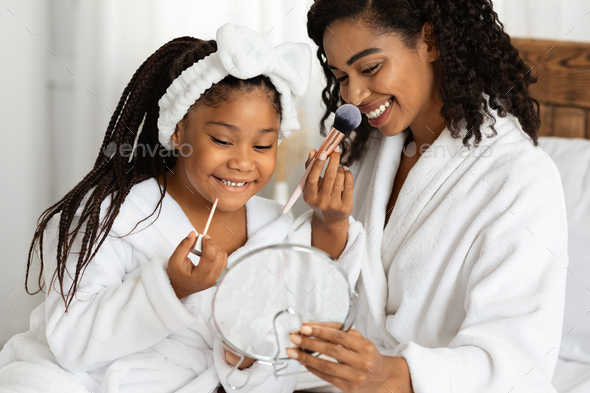 African Mom And Daughter In Bathrobes Holding Magnifying Mirror And Doing Makeup