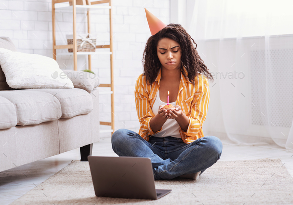 Sad black woman in party hat celebrating birthday online alone