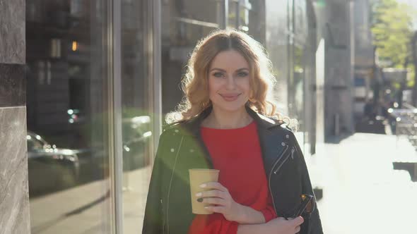 Stylish Beauty Smiles at the Camera While Standing on the Street Near a Modern Office Building alt