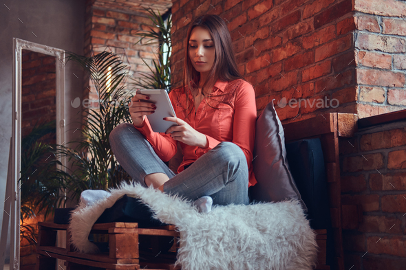 A charming brunette in casual clothes with a tablet sitting in a - Stock Photo - Images