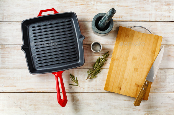 Empty cast iron pan and cutting board on a light wooden background, top view, copy space.