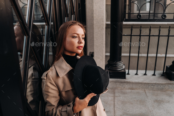 Stylish young woman in a beige coat in a black hat on a city street. Women's street fashion - Stock Photo - Images