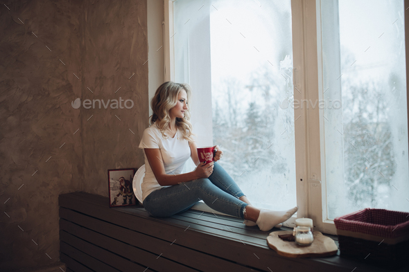 Beautiful blonde sitting on window sill with mug. - Stock Photo - Images