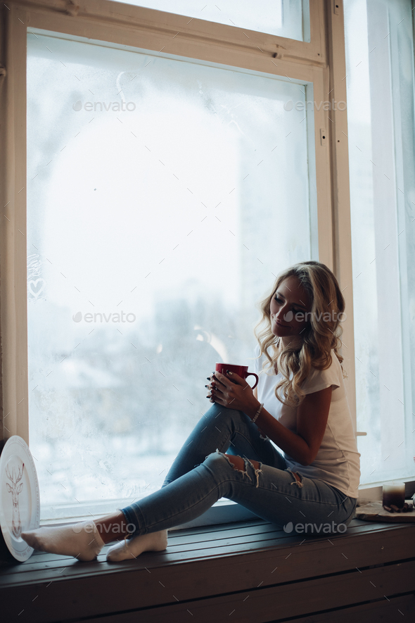 Beautiful blonde sitting on window sill with mug. - Stock Photo - Images