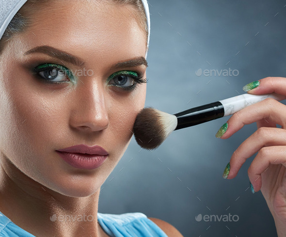 Pretty woman with green makeup drawing blush for herself.