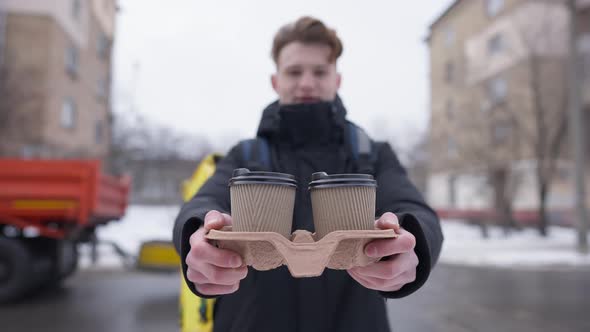 Blurred Young Courier Stretching Disposable Paper Coffee Cups at Camera Standing Outdoors on Cold alt