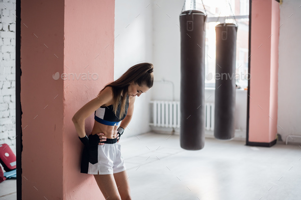 The female athlete was tired in training and leaned against the wall to rest.