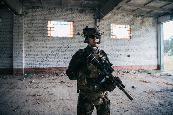 Military man with assault rifle standing inside building, he is ready for combat.
