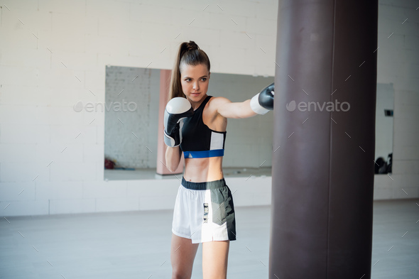 A girl in sports clothes is engaged in boxing and works out a punch with her hand on a punching bag