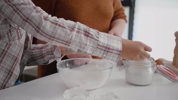 Grandmother Teaching Granddaughter How to Sift Flour Using Kitchen Strainer alt