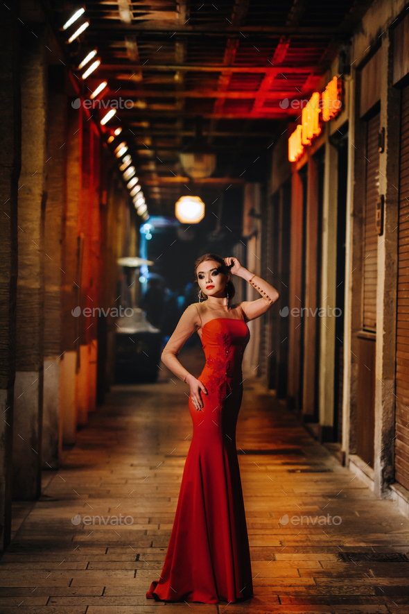 An elegant girl in a red evening dress on the streets of the night city of Marseille.A woman in a