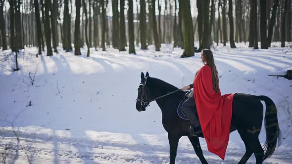 Real Time Video of Long Haired Charming Female Wearing Red Cloak Riding Black Stallion Past Camera alt