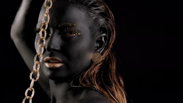 Closeup of a Woman with Black and Gold Paint and a Gold Chain Posing in Studio alt