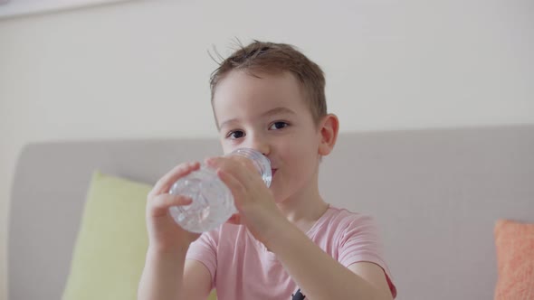 Cute Boy Drinks Water From a Bottle Sitting on the Couch at Home alt