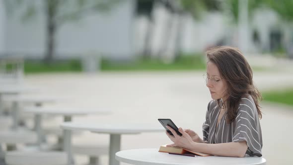 Contemporary Townswoman is Studying with Book and Smartphone in Park at Summer alt