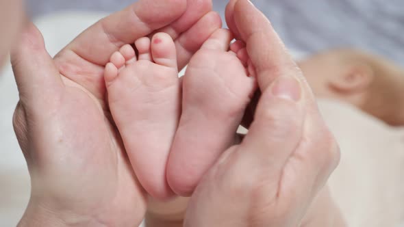 Mother Holds Tiny Pink Feet of Newborn Daughter on Bed alt