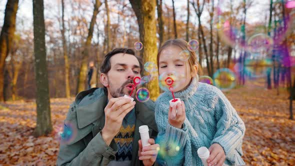 Young Dad and Little Daughter Blowing Soap Bubbles Which Flying on you alt