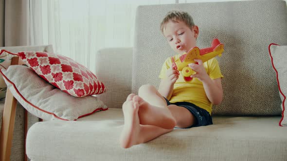 A Cute Little Preschooler Boy Playing at Home on the Sofa with a Toy Airplane a Cute Little Son alt