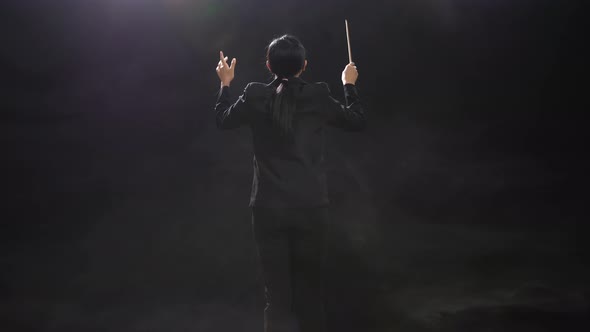 Back View Of Asian Conductor Woman Holding A Baton And Showing Gesture Quickly In The Black Studio alt