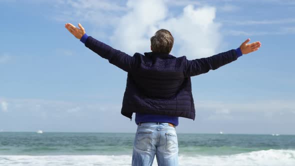 Mature man standing with arms outstretched on the beach alt