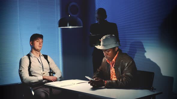 Multiracial Desperate Criminal Writing Last Message on Smartphone in Interrogation Room. alt