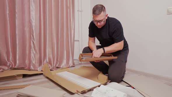 a Young Man in Glasses Takes Out of the Box Parts for Assembling a Chest of Drawers alt