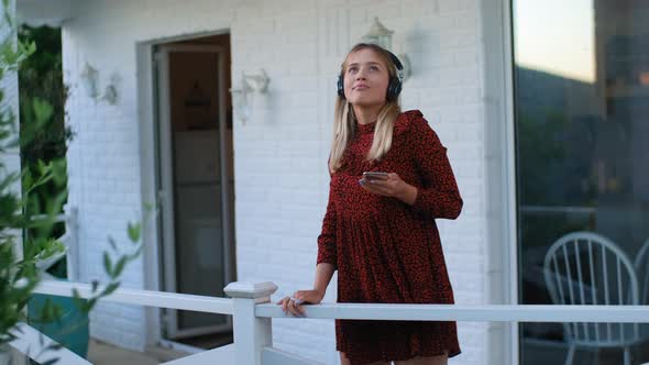 Young Woman Standing on Terrace Balcony Listen to Music in Wireless Headphones and Dance alt