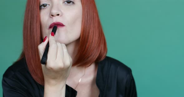 Focus on Beautiful and Confident Red Haired Woman Looking at Camera and Drawing Lips By Red Lipstick