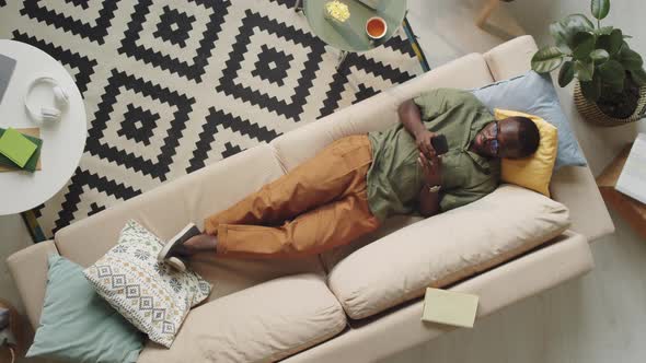 Afro-American Man Lying on Couch and Using Smartphone alt