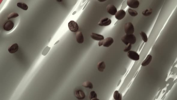 Flying coffee beans mix into flowing milk in slow motion