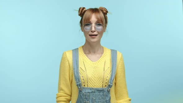 Attractive Young Woman with Bangs and Buns Hairstyle Wearing Sunglasses with Yellow Sweater Raising