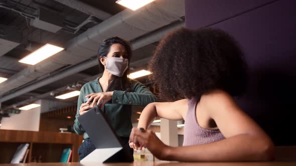 Two Businesswomen In Masks Have Socially Distanced Meeting In Office Touching Elbows During Pandemic